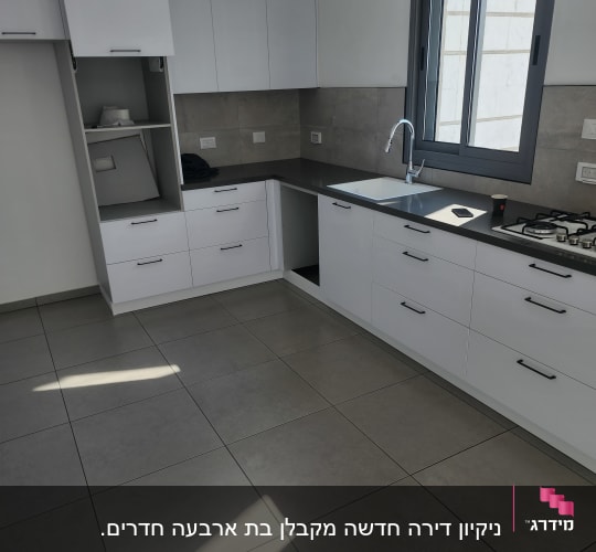 מטבח נקי עם ארונות לבנים ומשטח עבודה אפור